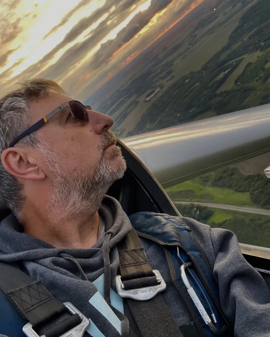 Michael Sønderup Nielsen i cockpittet under et drej i aftensol, med vingen og landskabet i baggrunden