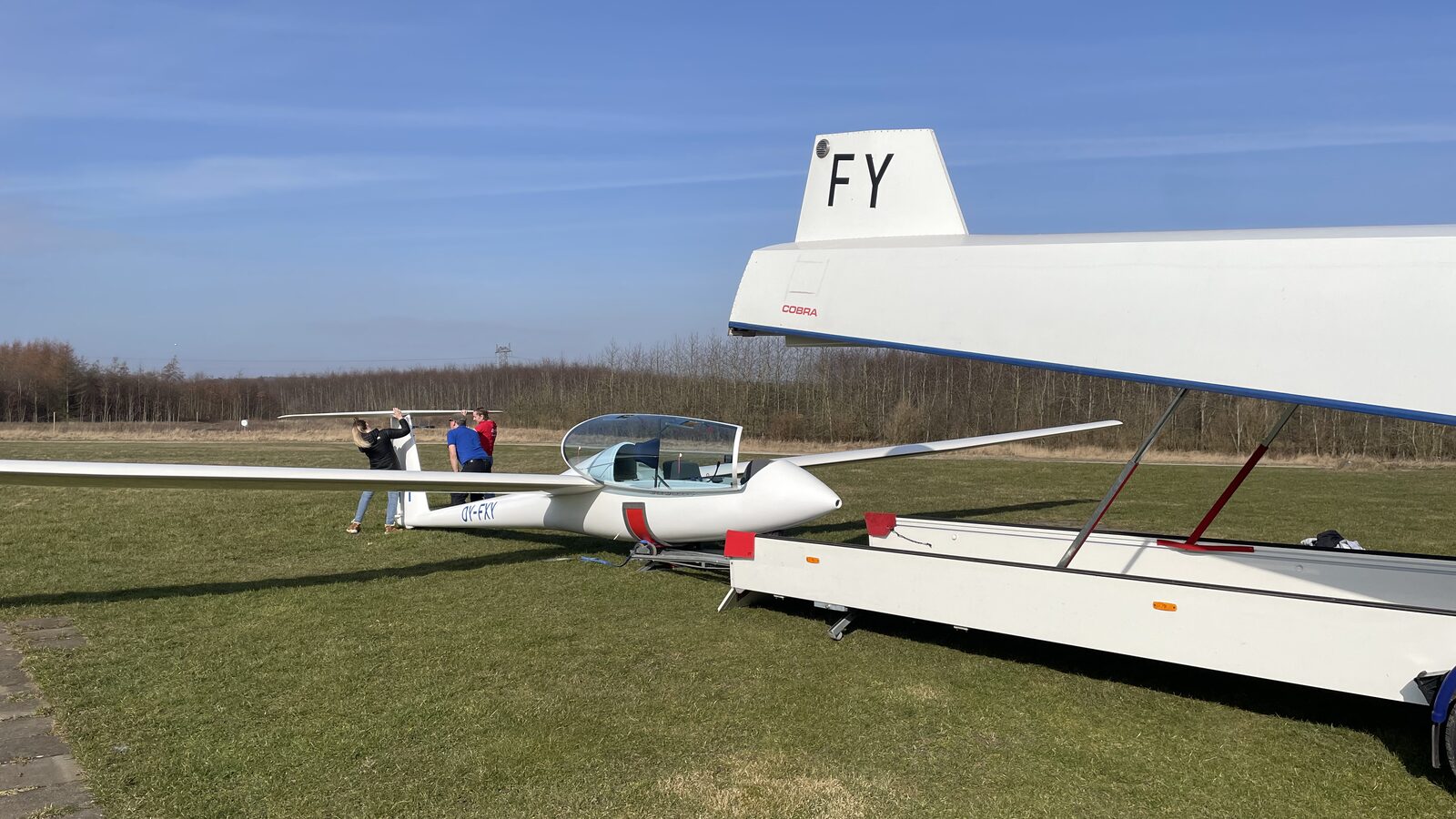 Motorsvævefly og svævefly på græsset med medlemmer omkring