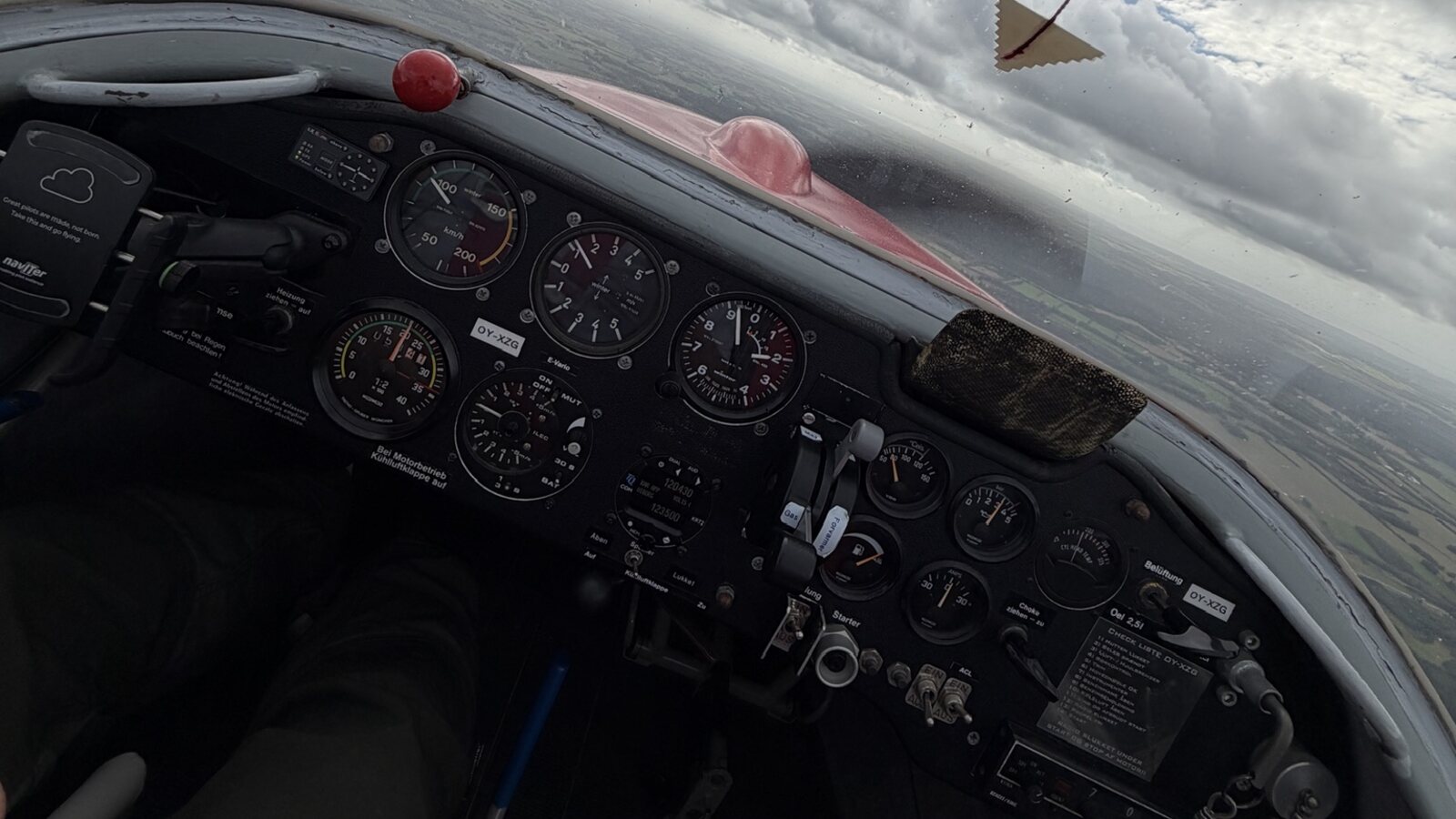 Udsigten fra cockpittet i klubbens motorsvævefly med instrumentbrættet i forgrunden og skydækket over horisonten